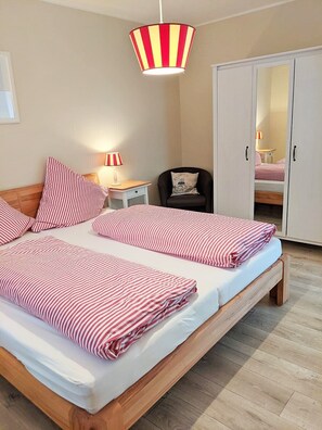 Ein Schlafzimmer mit einem Bett, Nachttischen, einer Lampe, einem Sessel, einem Kleiderschrank und einer deckenhohen Leuchte mit Streifenmuster.