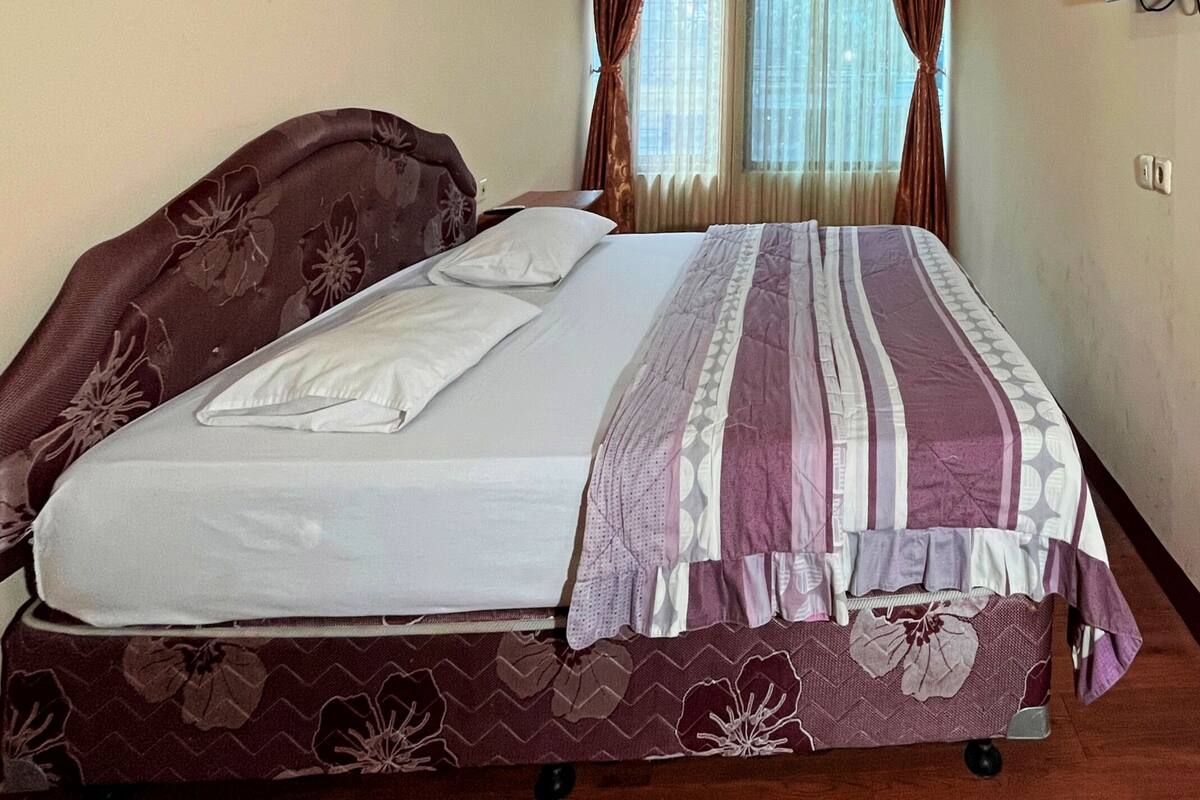 Una cama individual con una colcha estampada, un televisor en la pared y una ventana con cortinas.