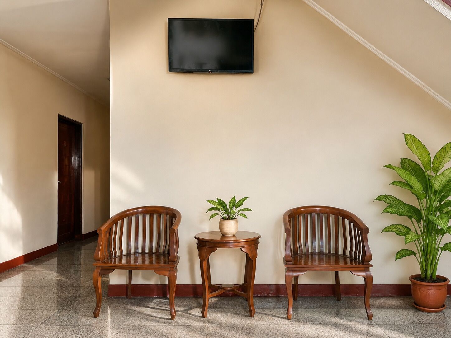 A hallway with two wooden chairs, a small table with a potted plant, and a large potted plant.
