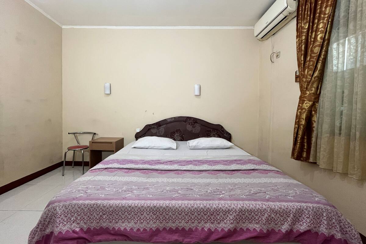 Un dormitorio con cama, una silla, un escritorio y un equipo de aire acondicionado.
