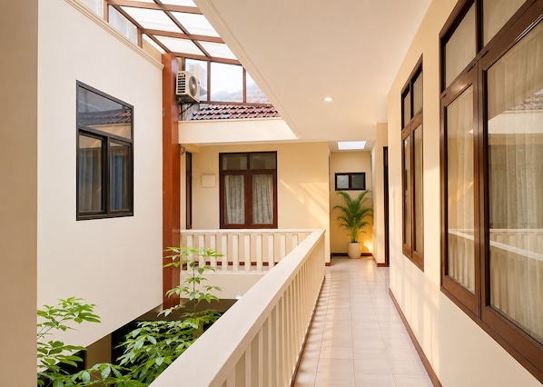 A narrow corridor with a balcony, a potted plant, and a window with curtains. - Hotel Bandung Indah (Bandung)
