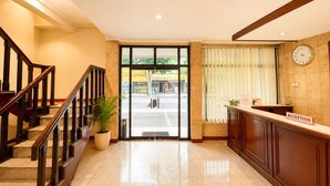A hotel reception area with a staircase, a reception desk, a clock, and a large glass door leading outside. - Hotel Bandung Indah (Bandung)