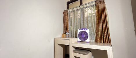A corner room with a desk, a chair, a fan, and a window with curtains.