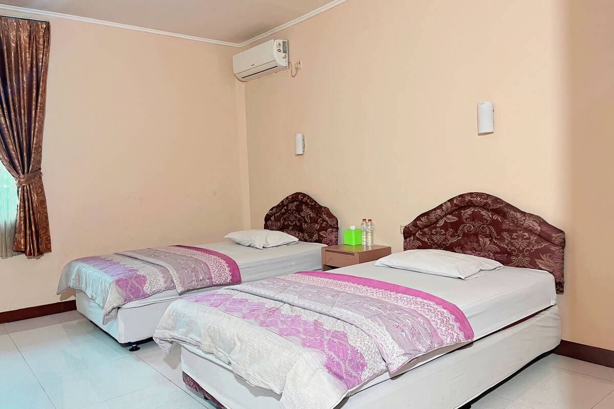 Habitación de hotel con dos camas, una mesita de noche, un equipo de aire acondicionado y una ventana con cortinas.