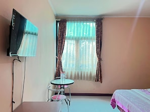 Ein Hotelzimmer mit Fernseher, einem runden Tisch mit Stühlen, einem Bett und einem Fenster mit Vorhängen.