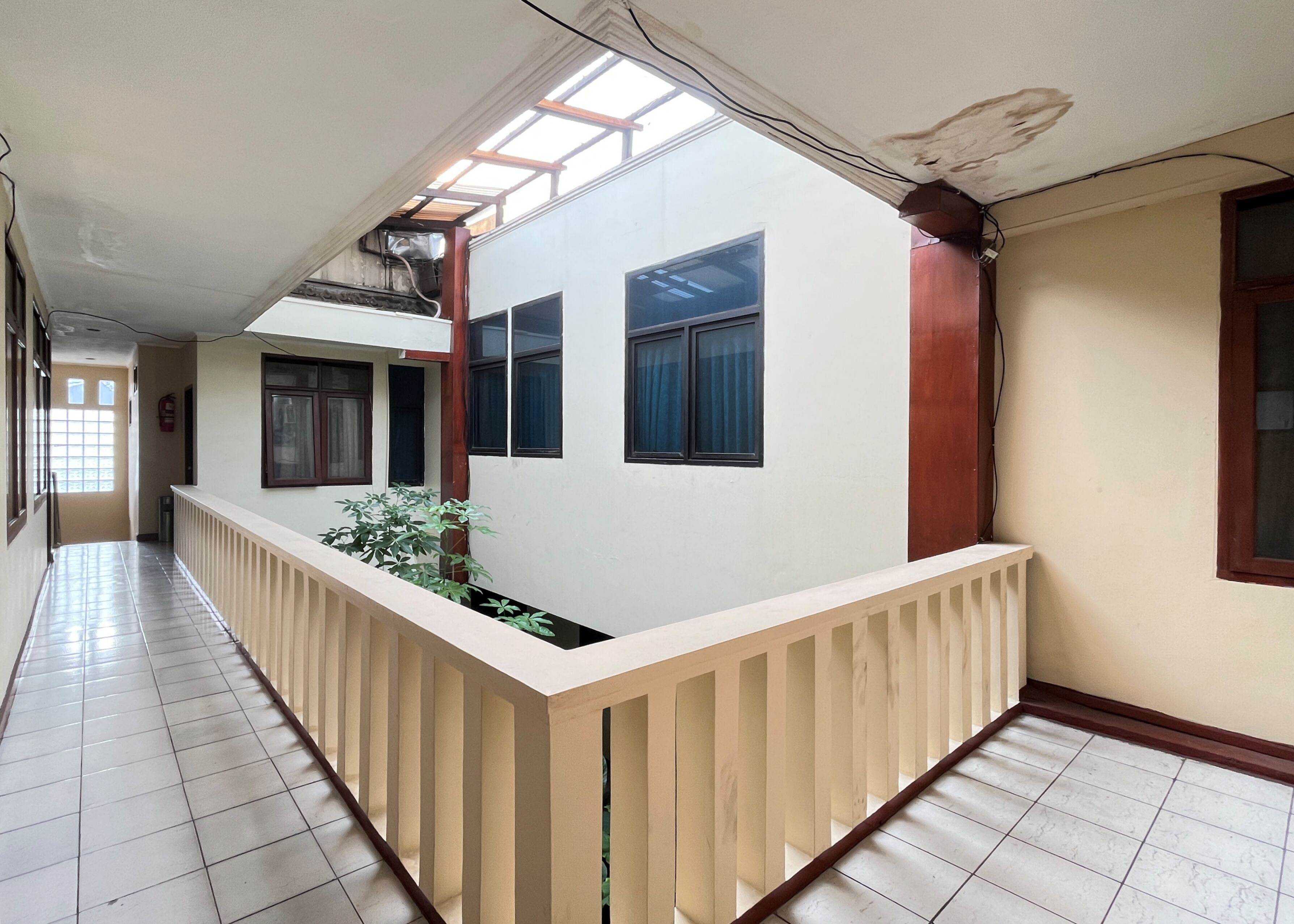 A corridor with a tiled floor, a wooden railing, and a window with a view of the sky.