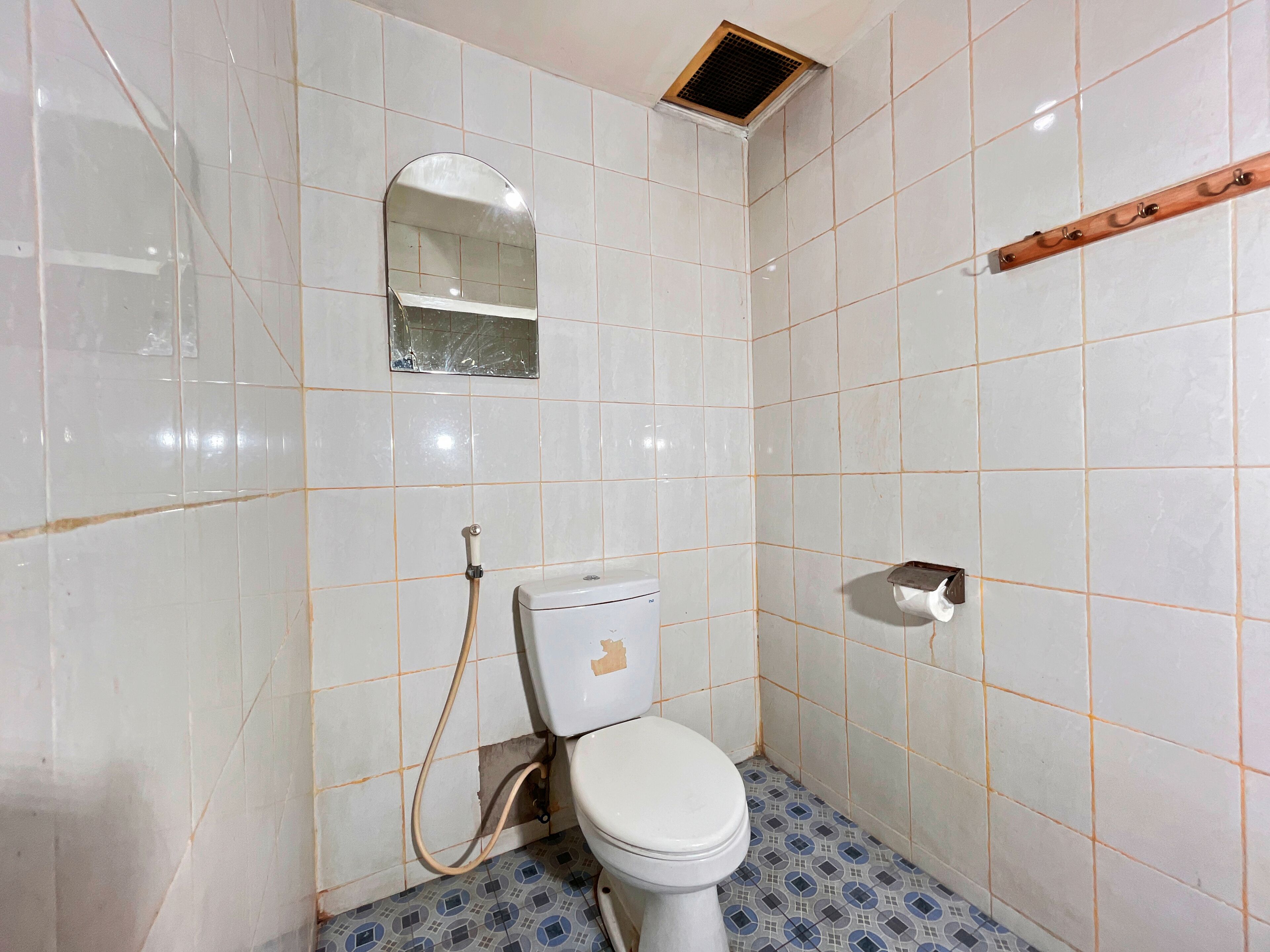 A bathroom with white tiled walls, a toilet, a shower, and a mirror.