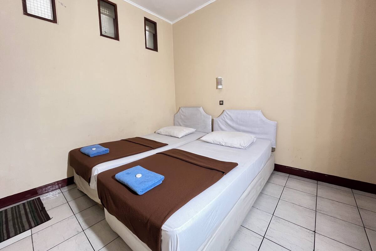 Habitación de hotel con dos camas, una ventana, una lámpara de pared y suelo de baldosas.