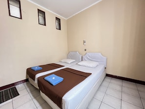 A hotel room with two beds, a window, a wall-mounted light, and a tiled floor. - Hotel Bandung Indah (Bandung)