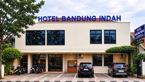 A hotel with a modern facade, a reception area, and a parking lot with several cars and motorcycles. - Hotel Bandung Indah (Bandung)