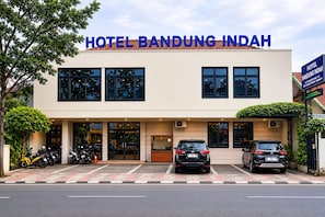 A hotel with a modern facade, a reception area, and a parking lot with several cars and motorcycles. - Hotel Bandung Indah (Bandung)