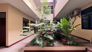 A spacious indoor area with a central planter filled with large leafy plants, a tiled floor, and a high ceiling with a skylight. - Hotel Bandung Indah (Bandung)