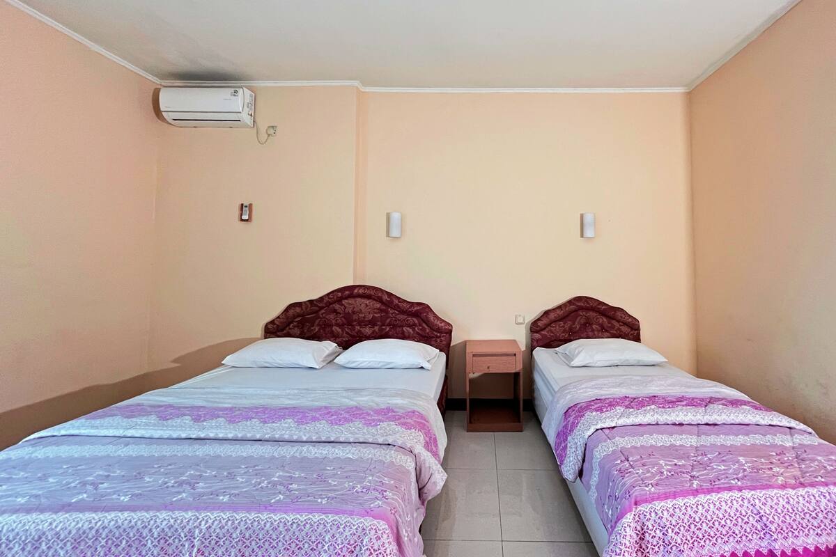 Una habitación con dos camas, aire acondicionado en la pared y lámparas de noche.