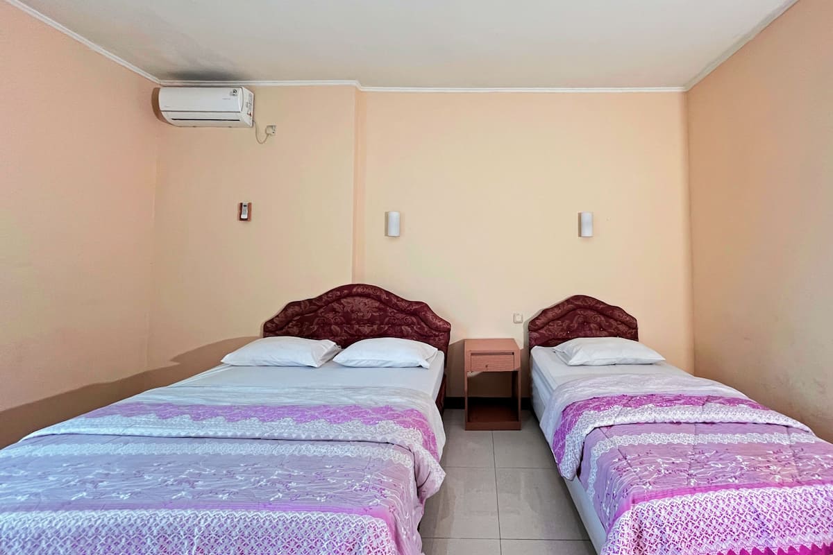 A room with two beds, a wall-mounted air conditioner, and bedside lamps.