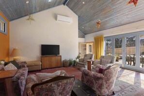 A living room with a flat-screen TV, wooden cabinet, floral-patterned sofas, and a large sliding glass door leading to an outdoor area. - El Dorado | Sunny Family Home, Walk to Town (Katoomba)