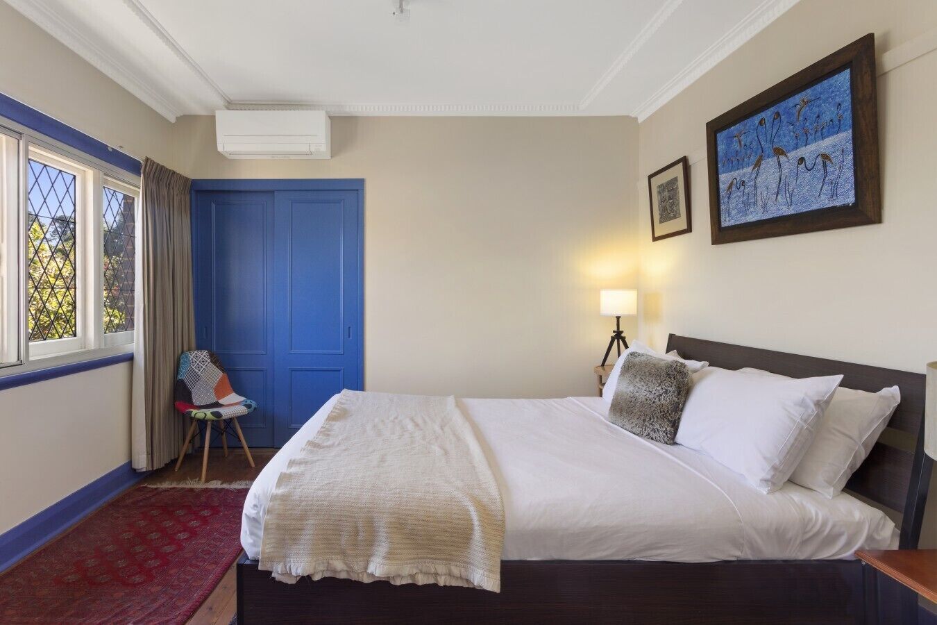 A hotel room with a bed, a chair, a desk, a lamp, and a painting on the wall.