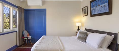 Habitación de hotel con cama, una silla, escritorio, lámpara y un cuadro en la pared.