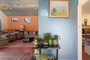 A living room with a sofa, a coffee table, and potted plants. There is a painting on the wall and a star decoration on the ceiling. - El Dorado | Sunny Family Home, Walk to Town (Katoomba)