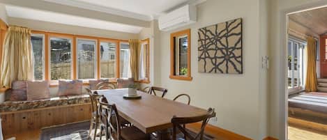 Un comedor con una mesa y sillas de madera, un banco con cojines y vistas a través de amplias ventanas.