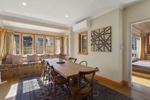 A dining area with a wooden table and chairs, a bench with cushions, and a view through large windows. - El Dorado | Sunny Family Home, Walk to Town (Katoomba)