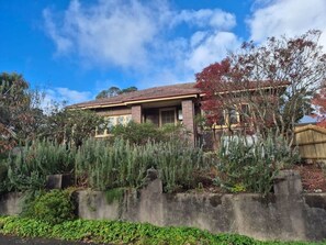 Ein zweigeschossiges Haus mit Backsteinfassade, einer Veranda und einem Garten mit verschiedenen Pflanzen.