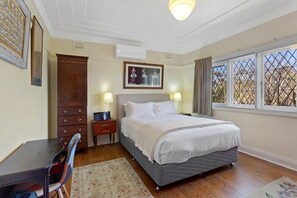 A bedroom with a bed, bedside tables, a desk, a chair, a window with a view, and a ceiling light. - El Dorado | Sunny Family Home, Walk to Town (Katoomba)
