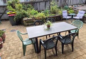 Eine Terrasse mit Tisch und Stühlen, umgeben von Kübelpflanzen und einem Holzzaun.