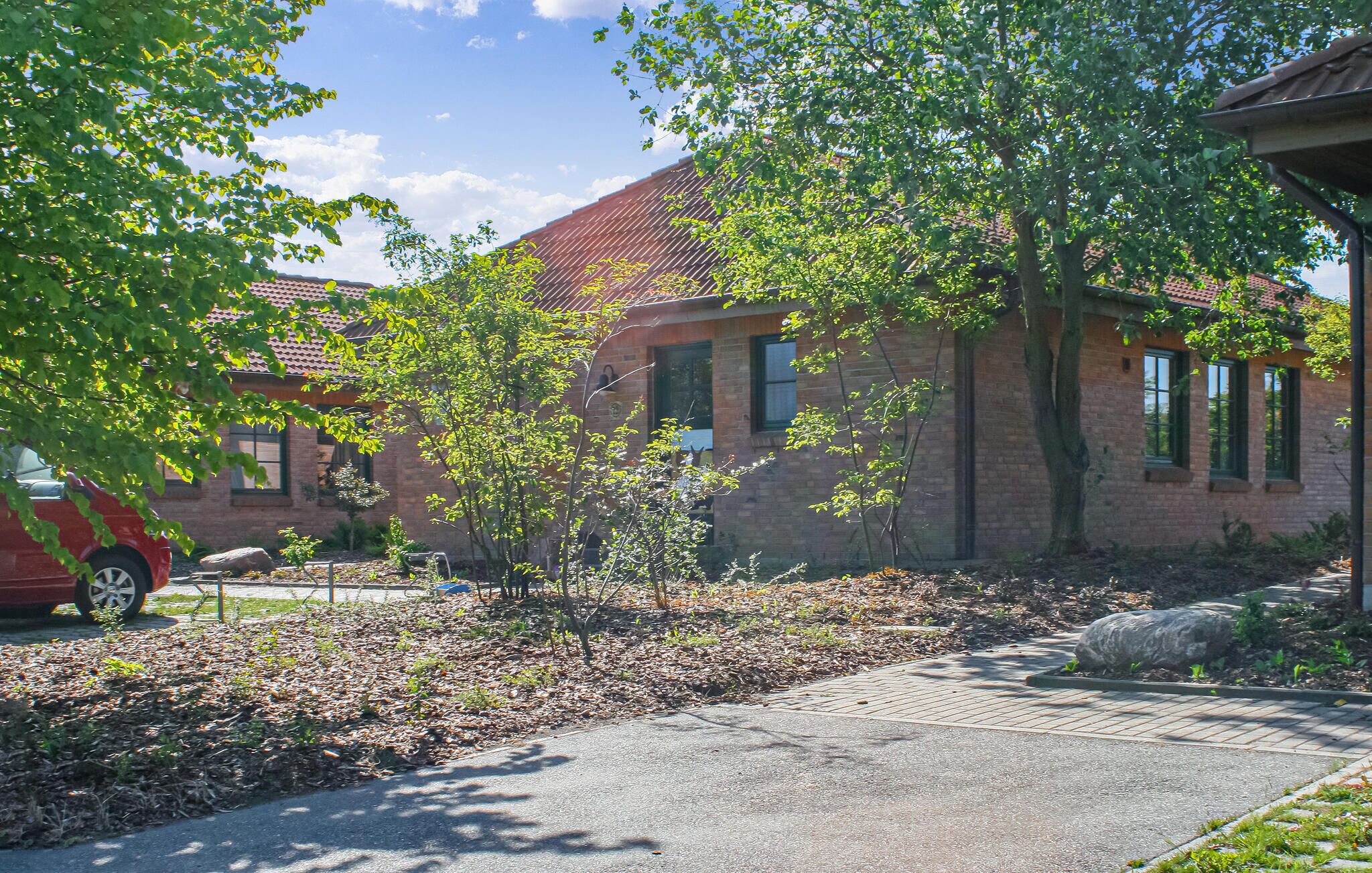 A brick building with a red car parked in front, surrounded by trees and a paved driveway.