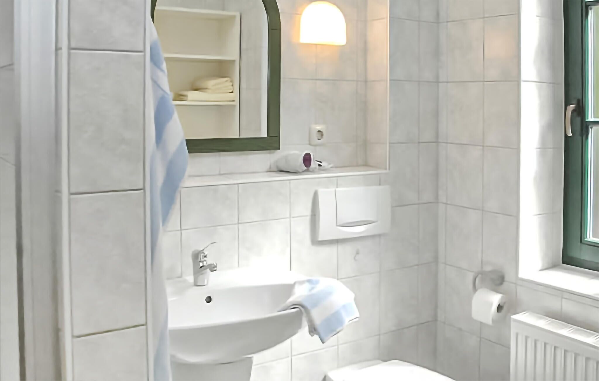 Un baño con lavamanos, espejo, toallero y ventana.