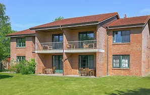 Ein zweistöckiges Backsteingebäude mit einem Balkon im zweiten Obergeschoss, großen Fenstern und einem gepflegten Rasen.