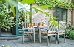 Eine Terrasse im Freien mit Tisch und Stühlen, einer Ziegelwand und viel Grün.