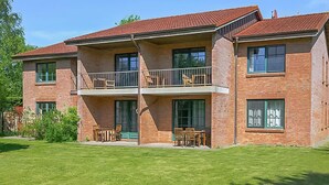 Ein zweistöckiges Backsteingebäude mit einem Balkon im zweiten Obergeschoss, großen Fenstern und einem gepflegten Rasen.
