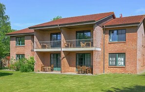 Ein zweistöckiges Backsteingebäude mit einem Balkon im zweiten Obergeschoss, großen Fenstern und einem gepflegten Rasen.
