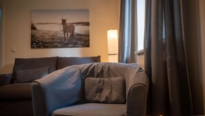 En stue med en sofa, en lænestol, en lampe og et maleri på væggen.