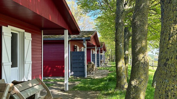 En række hytter med røde facader og hvidt pyntværk, træbænke og en belagt sti.