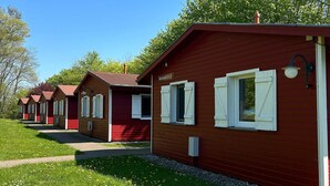 En række træhytter med hvide skodder, en klar himmel og en græsplæne foran.