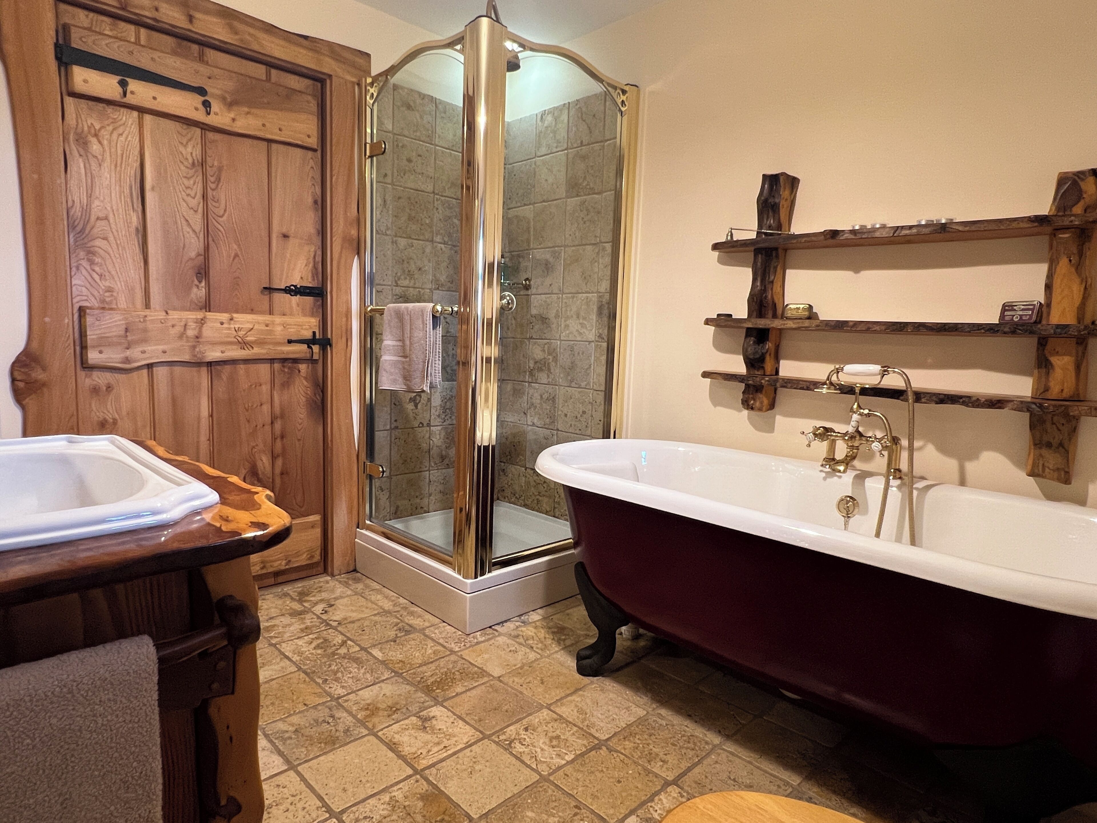 Un baño con una bañera independiente, ducha con mampara de cristal y estanterías de madera.
