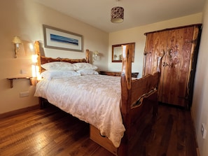 A bedroom with a wooden bed, bedside lamps, a nightstand, a wooden wardrobe, and a framed picture on the wall. - 5 Star Traditional Hebridean Thatched Cottage  Isle of South Uist awaits you (Isle of South Uist)