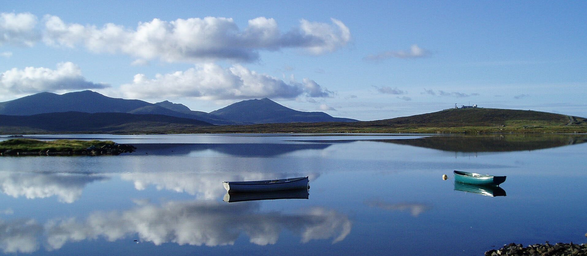 Un lago tranquilo con montañas al fondo, un pequeño bote sobre el agua y un cielo despejado.
