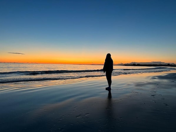 Une personne se promenant sur une plage au coucher du soleil.