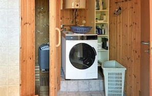 A laundry area with a washing machine, a dryer, a blue basket, and a white laundry basket. - Stunning home in Kalundborg with sauna (Kalundborg)