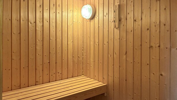 Una panca in legno all'interno di una sauna, con una lampada sulla parete.