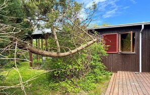 A wooden cabin with a red window shutter, surrounded by dense greenery and a wooden deck. - Stunning home in Kalundborg with sauna (Kalundborg)