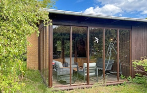 A modern glass-enclosed patio with outdoor furniture, a wooden deck, and a view of the surrounding greenery. - Stunning home in Kalundborg with sauna (Kalundborg)