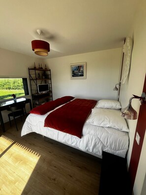 Ein Schlafzimmer mit einem Bett, einem Schreibtisch mit Computer, einem Fernseher und einem Bild an der Wand.