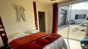 Ein Schlafzimmer mit einem großen Bett, einer Deckenleuchte, einer an der Wand befestigten Engeldekoration und Blick auf eine Terrasse.