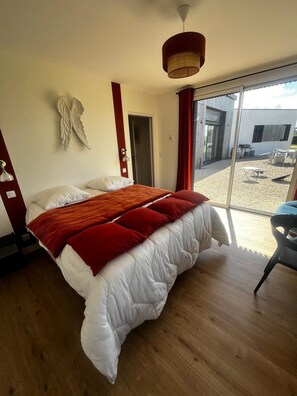 Ein Schlafzimmer mit einem großen Bett, einer Deckenleuchte, einer an der Wand befestigten Engeldekoration und Blick auf eine Terrasse.