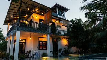 A two-story building with a balcony, a pool, and a well-lit entrance.