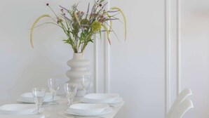 Ein Esstisch mit einer weißen Blumenvase, weißen Tellern und Gläsern.