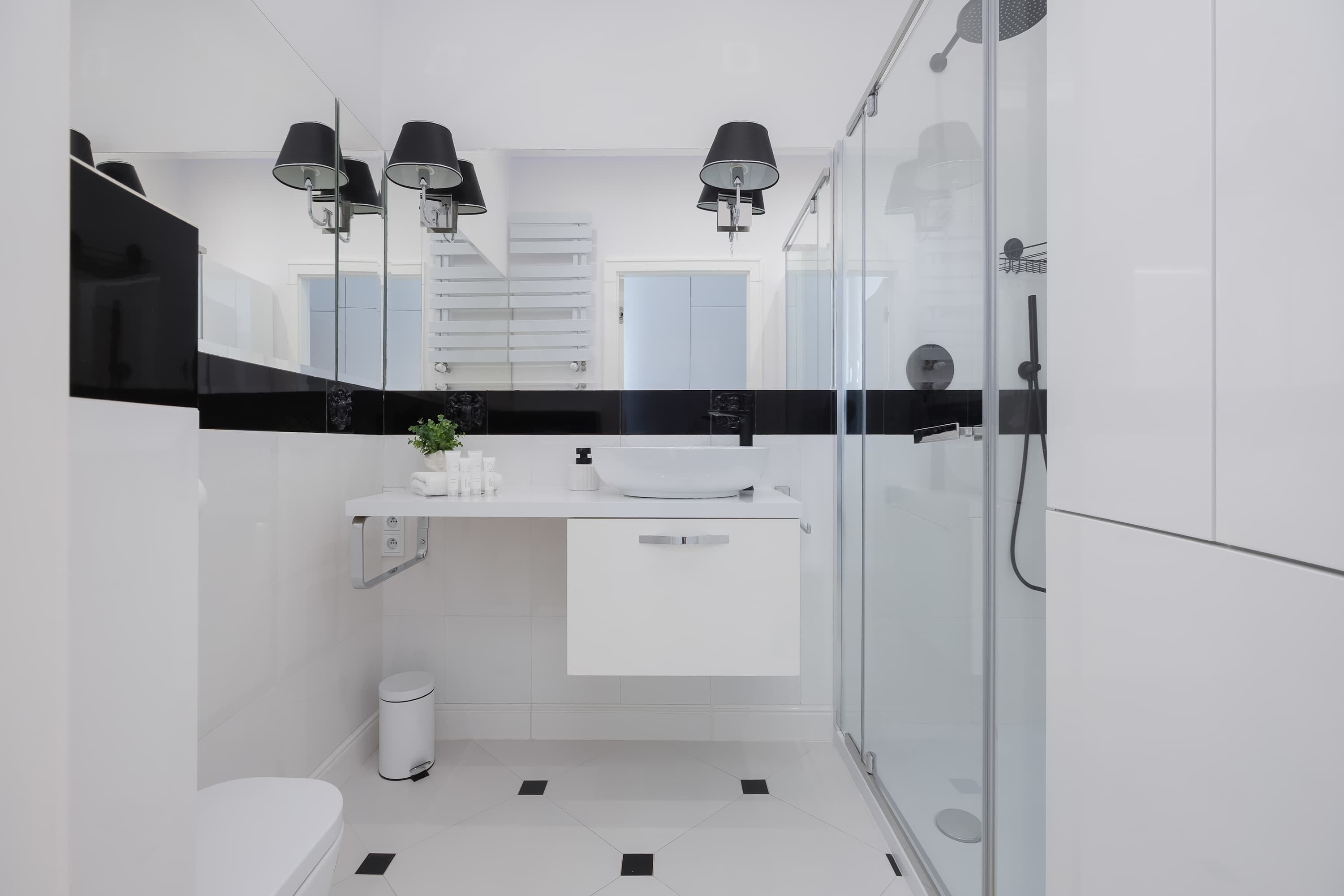 Ein modernes Badezimmer mit einem weißen Waschbecken, einer schwarzen Arbeitsplatte und einer Duschkabine aus Glas.